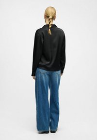 Camisa larga de satén negra de manga larga combinada con pantalones anchos de mezclilla ligera y azul claro, con un diseño sencillo y una silueta casual.