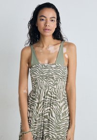 Green and beige dress featuring a fitted bodice with a zebra pattern, wide straps, and a flowing skirt with an elasticized waist.