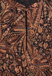 Tissu noir ornée de motifs paisley et floraux complexes dans des tons d'orange, de crème et d'or, avec un détail de bouton au niveau de l'encolure.