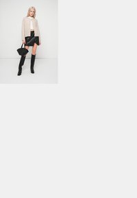 Bež kardigan, bel crop top, črna mini krila iz umetnega usnja, črne visoke škornje in črna torbica. Preprost dizajn, gladka tekstura.