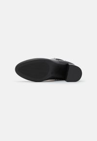 Musta kenkä, jossa on sileä pinta, lohkopohja, kuvioitu pohja ja minimalistinen muotoilu. Ominaisuuksiin kuuluu vankka rakenne ja hillitty logodetaili.