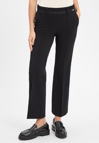 Zwarte wijde broek gemaakt van gestructureerde stof, met een gladde tailleband, zijzakken en een nette pasvorm. Gecombineerd met zwarte loafers.
