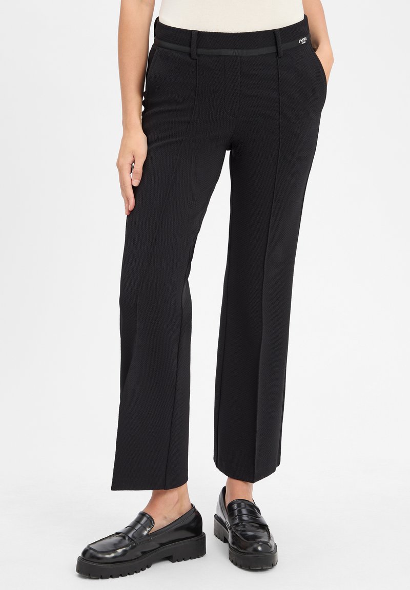 Zwarte wijde broek gemaakt van gestructureerde stof, met een gladde tailleband, zijzakken en een nette pasvorm. Gecombineerd met zwarte loafers.