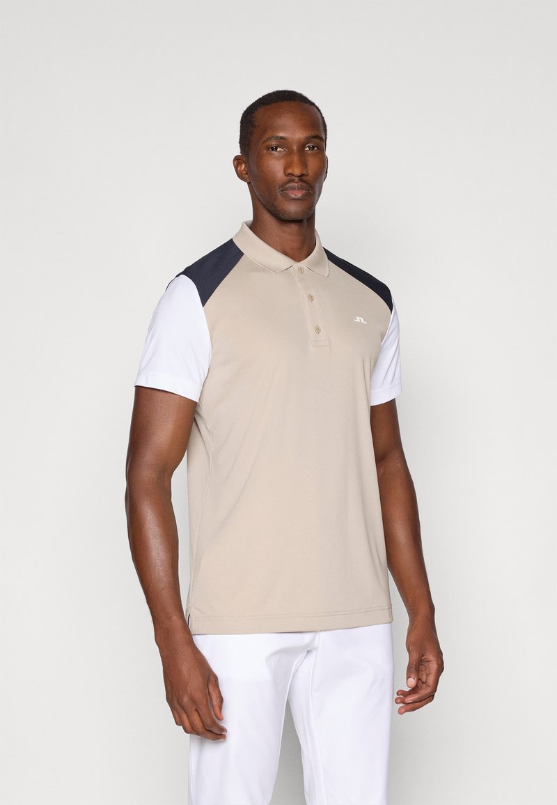 Polo bege com acentos nos ombros em azul-marinho e mangas curtas brancas. Feito de um tecido suave, apresenta colarinho e uma patilha com três botões.