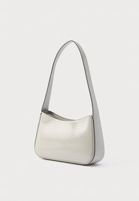 Borsa a tracolla in pelle verniciata grigia dal design curvo, caratterizzata da una tracolla sottile e una finitura lucida. Rifinita con un colore a contrasto.