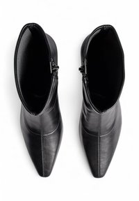 Botas de tobillo de cuero negro con punta afilada, textura suave y cremallera lateral. Cuenta con costuras visibles a lo largo de la parte superior.