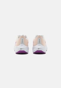 Zapatillas de running ligeras con parte superior de malla en rosa suave, detalles en blanco, talón gris y suela de goma morada. Logotipo de Nike visible.