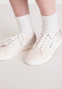 Sneakers in tela rosa chiaro con suole in gomma bianca, dotati di lacci bianchi e un accento con logo. Indossati con calze bianche a coste.