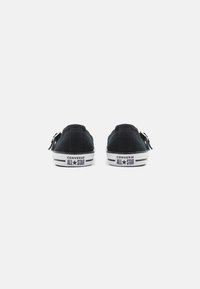 Czarne płócienne trampki mają niski krój, białe gumowe podeszwy oraz charakterystyczną etykietę na języku. Tył prezentuje markę Converse oraz detale faktury.