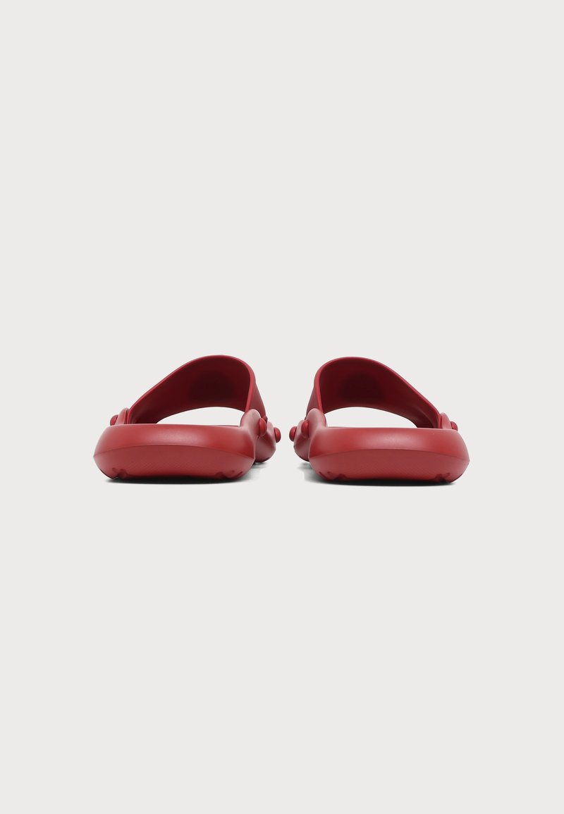 Paar rote Slip-On-Sandalen mit abgerundeten Sohlen und breiten Riemen, von hinten auf weißem Hintergrund dargestellt.