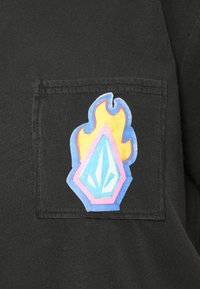 Μαύρο T-shirt με πολύχρωμο σχέδιο φλόγας και μπλε διαμάντι ραμμένα πάνω στην περιοχή της αριστερής τσέπης στο στήθος.