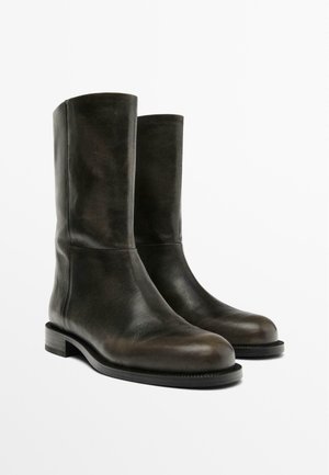 Hnědé kožené kotníkové boty s hladkým povrchem, kulatou špičkou a plochou podrážkou. Jednoduchý design s mírně zvýšeným podpatkem a bez viditelného kování.