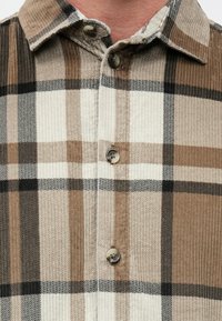 Καφέ και εκρού καρό πουκάμισο από κορδόνι με γιακά και κουμπιά, με υφή και αντίθετες οριζόντιες και κάθετ�ες γραμμές.