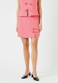 Rosa, tettsittende to-delt antrekk med ermeløs topp med sløyfedetaljer og miniskjørt med sidesplitter og matchende sløyfedetaljer.