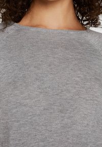 Hellgrauer Pullover mit strukturiertem Rippenmuster, weitem Ausschnitt und Raglanärmeln, aus weichem Strickstoff gefertigt.