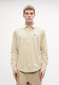 Beige overhemd met knoopjes en een subtiel geometrisch patroon, lange mouwen en een zwart "BOSS" logo op de borst. Soepele stofstructuur.