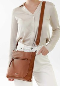 Braune Leder-Umhängetasche mit einer strukturierten Oberfläche, einem vorderen Reißverschlussfach und einem verstellbaren Trageriemen. Das Design ist schlicht und funktional.