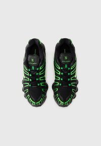 Black athletic shoes featuring a mesh upper with bright green accents and a distinctive sole design. Laces and padded collar complete the look.