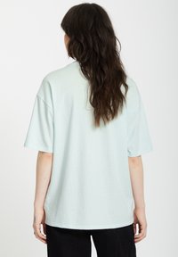 Hellblaue Oversized-T-Shirt aus einem weichen Material. Kurze Ärmel und ein runder Ausschnitt. Hat einen geraden Schnitt mit seitlichen Schlitzen.