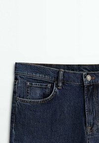 Jean en denim bleu foncé avec poche avant, passants pour ceinture et fermeture par bouton métallique sur fond blanc.