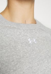 Sudadera gris hecha de un tejido suave que presenta un escote acanalado y un logo de Under Armour en blanco en el pecho. Vista en primer plano de la textura.