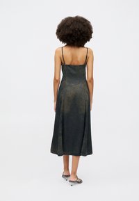 Vestido midi de denim com alças finas, lavagem escura e ligeira evasé na bainha. Apresenta uma superfície texturizada com áreas desbotadas no tecido.