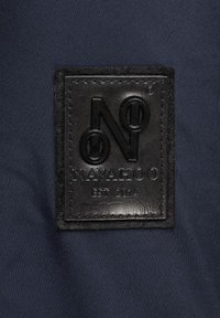 Black leather label with embossed "N" and "NAVAHOO EST 2014" text, stitched into navy fabric background. Textured surface with detailed stitching.