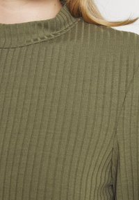 Olivgrünes geripptes Strickoberteil mit hohem Kragen, das vertikale Streifen, eine glatte Textur und eine taillierte Silhouette aufweist.