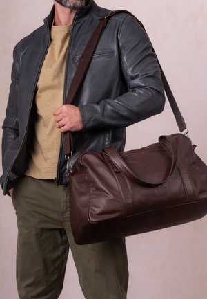 Brown leather duffel bag with dual handles, a detachable shoulder strap, smooth texture, and subtle stitching details.