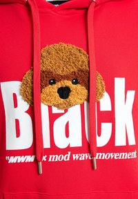 Sudadera roja con gran texto blanco que dice "Black". Presenta un parche con la cara de un perro marrón texturizado en la parte frontal. Cuerdas rojas con puntas plateadas.