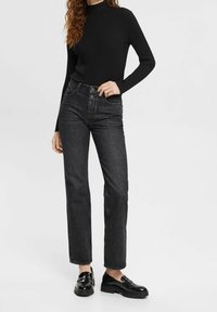 Musta ribattu pitkähihainen paita, jossa on korkeavyötäröiset suorat tummansiniset denim-farkut. Kiiltävät mustat loaferit paksuilla pohjilla viimeistelevät asun.
