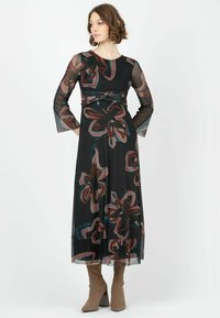 Langes schwarzes Kleid mit floralem Muster in burgunderrot und türkis, mit durchsichtigen langen Ärmeln und taillierter Taille. Kombiniert mit spitzen beigefarbenen Stiefeln.