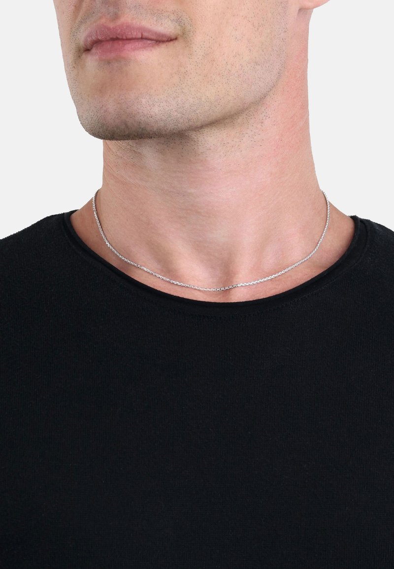 Silverkedja med en slät, vriden textur, bärs på en bar hals, som kompletterar en svart t-shirt med rund halsringning.