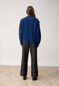 Niebieski sweter dzianinowy o prążkowanej fakturze i detalach na ramionach, połączony z ciemnoniebieskimi spodniami dżinsowymi o wysokim stanie z kontrastowymi szwami.