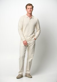Cremfarbener, langärmeliger Polopullover mit Kragen. Kombiniert mit hellen Hosen und beigen Sneakers, die aus strukturiertem Stoff bestehen.