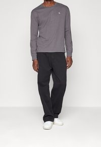 Harma pitkähihaine paita, jossa on pieni logo, yhdistetty löysiin mustiin housuihin ja valkoisiin tennareihin. Yksinkertainen muotoilu rentoa istuvuutta varten.