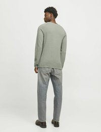 Grauer langärmeliger Pullover mit rundem Ausschnitt, kombiniert mit hellgrauen Jeans und dunklen Schuhen, von hinten betrachtet.