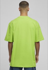 Kurzärmliges, oversized T-Shirt aus leuchtend grünem Baumwollstoff, mit rundem Ausschnitt und glatter Textur, mit geradem Schnitt am Saum.