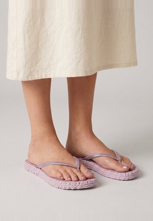 Feet wearing light purple woven flip-flop sandals and mauve nail polish, with a cream-colored skirt hem visible above ankles.