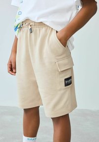 Beige shorts lavet af blødt stof, med elastisk talje, sidelommer og en cargo-lomme med en sort label akcent.