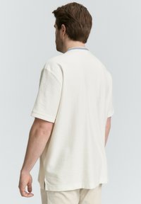 Kurzes, cremefarbenes Shirt aus strukturierter Stoffqualität, mit rundem Halsausschnitt und seitlichen Schlitzen am Saum für einen angenehmen Bewegungsfreiheit.