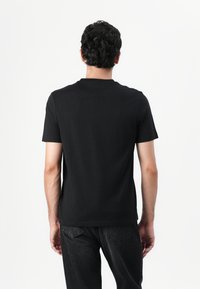 Zwarte katoenen T-shirt met korte mouwen, een ronde halslijn en een soepele textuur. De achterkant toont een korte snit en een eenvoudig ontwerp.