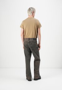 Tan kortlopende t-shirt gecombineerd met donkergrijze denim broek. De broek heeft een ontspannen pasvorm en zichtbare stikseldetails, met effen zwarte schoenen.
