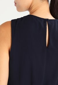 Námořnický bezrukávový top s výstřihem do V, měkká tkanina a klíčová díra na zadní straně, vybavená malým knoflíkovým uzávěrem.