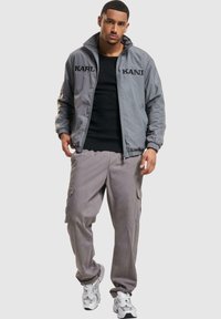 Gray bomber jacket with black lettering, paired with loose gray cargo pants and white sneakers. Smooth texture and relaxed fit.