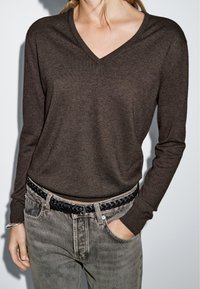 Brown V-neck sweater made of soft material, paired with faded gray jeans and a black braided belt, enhancing the overall casual look.