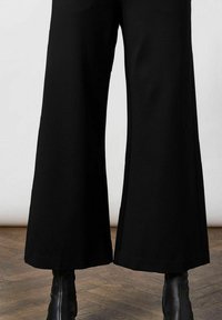 Zwarte wijde broek van soepel materiaal, met een hoge taille en uitlopende zoom, gecombineerd met stijlvolle zwarte enkellaarsjes.