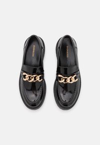 Zwarte lakleren loafers met een gouden kettingaccent aan de voorkant, met een ronde neus en een getextureerde zool.