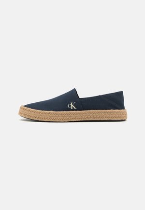Baskets en coton bleu marine à enfiler avec une semelle en jute tressé. Présente un logo CK discret sur le côté. Surface lisse et design simple.