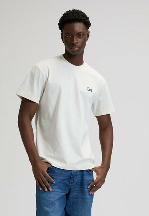 Biały bawełniany T-shirt z krótkimi rękawami i okrągłym dekoltem, z małym niebieskim logo "Lee" na piersi. Noszony z niebieskimi dżinsami.